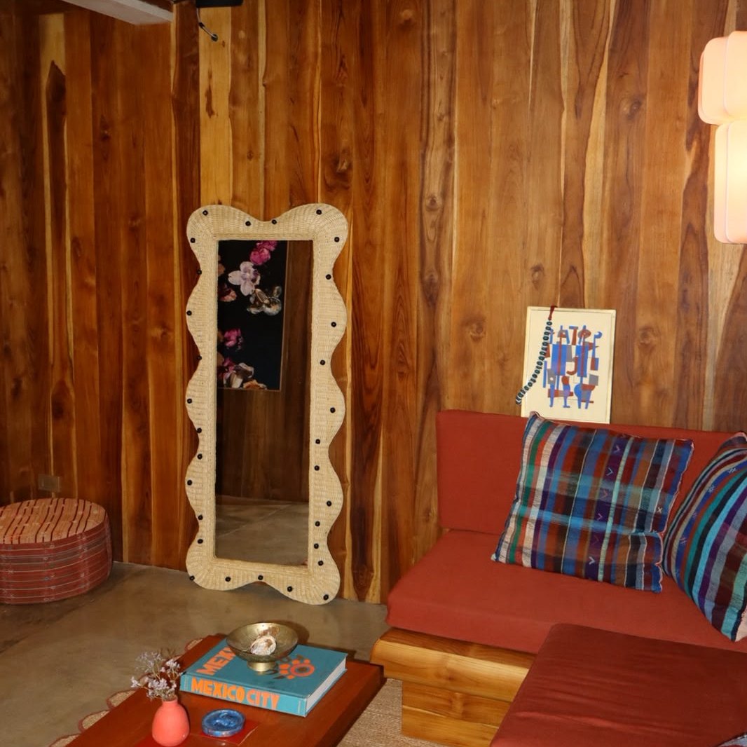 Wavy Cálamo mirror with black dots in a wood-paneled living room with a red sofa