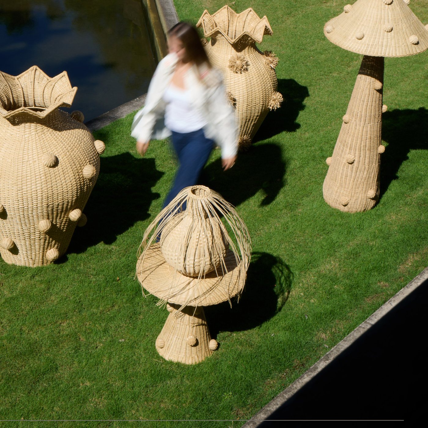 Large woven vases and a mushroom lamp on the grass by a pool