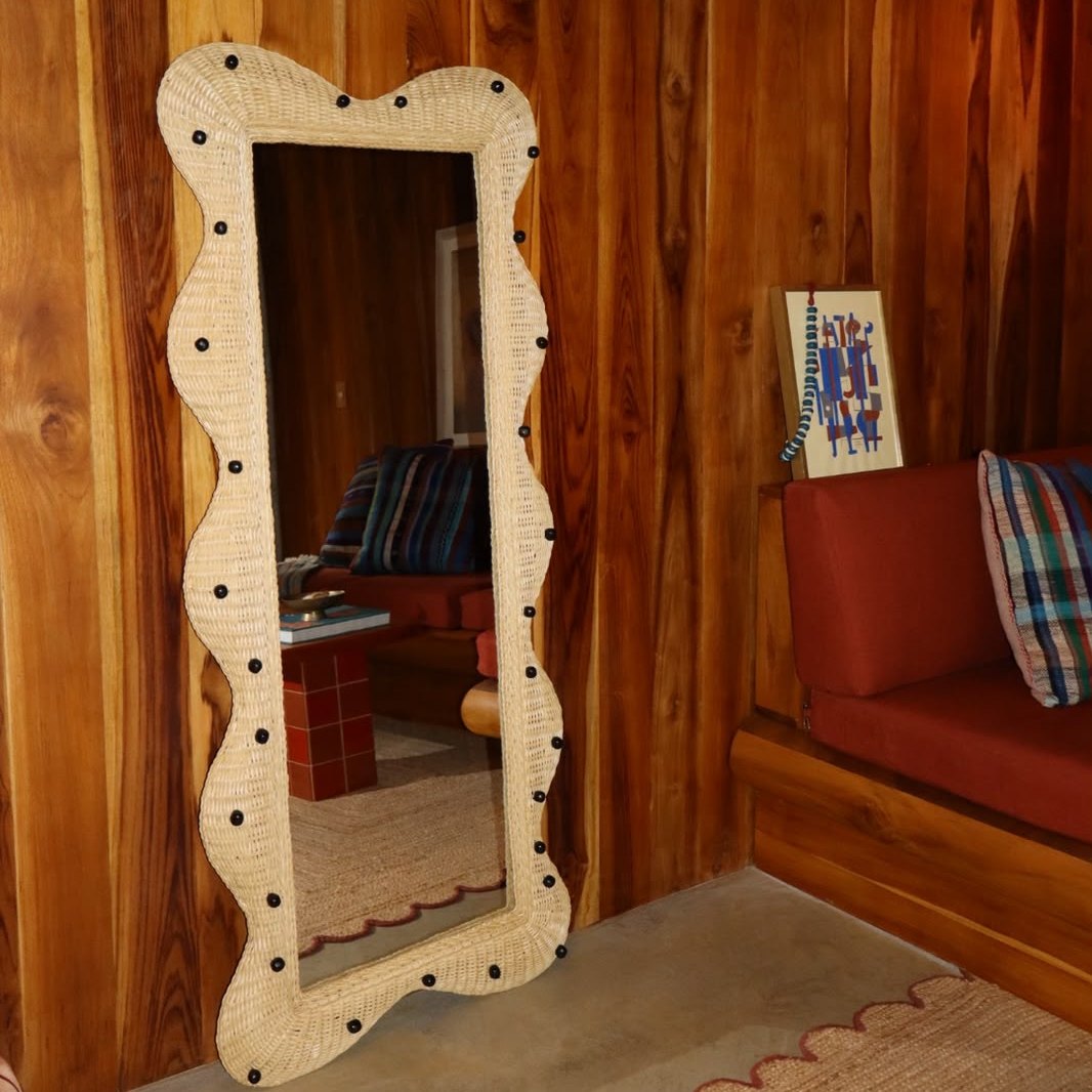 Close view of the wavy Cálamo mirror leaning against a wood wall
